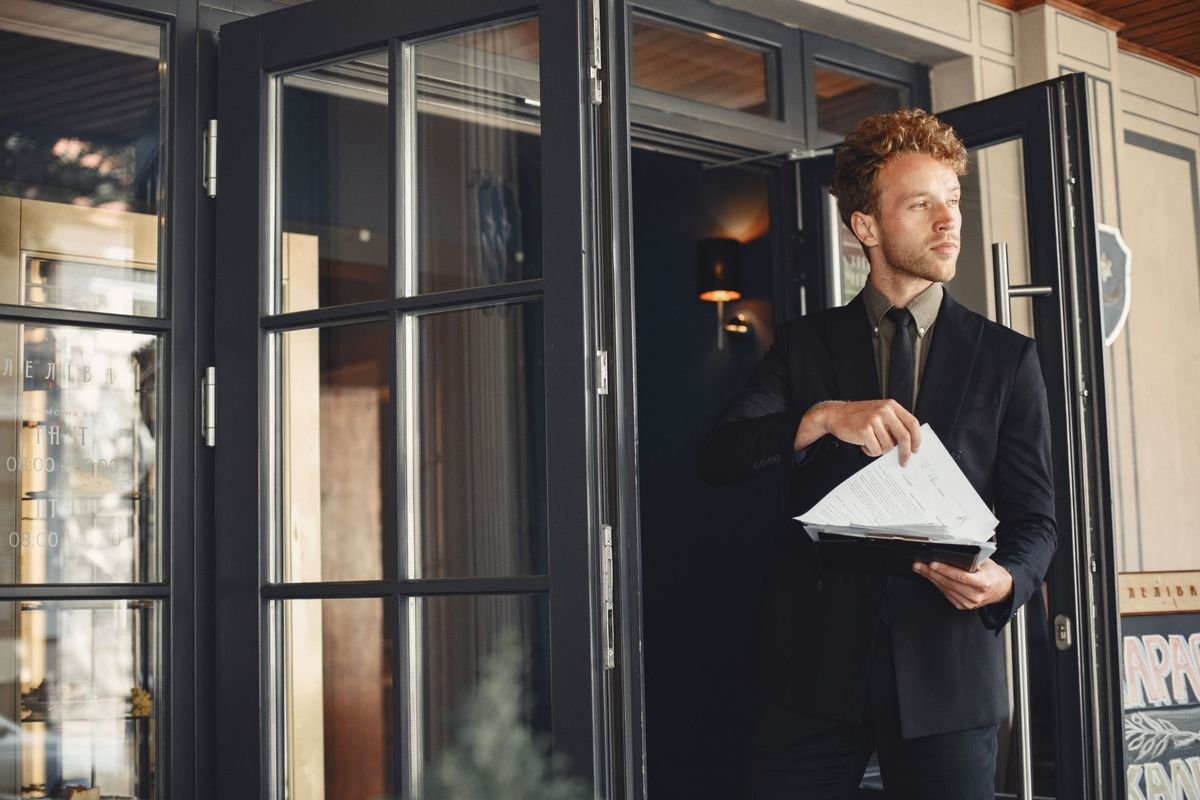 Ein Hoteldirektor im Anzug am Eingang seines Hotels.